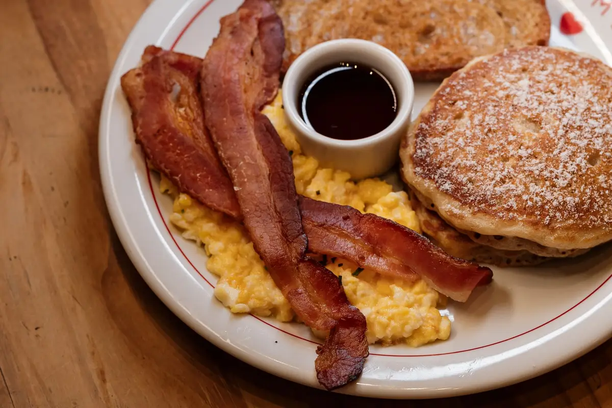 Diner breakfast plate with pancakes, bacon, scrambled eggs and syrup