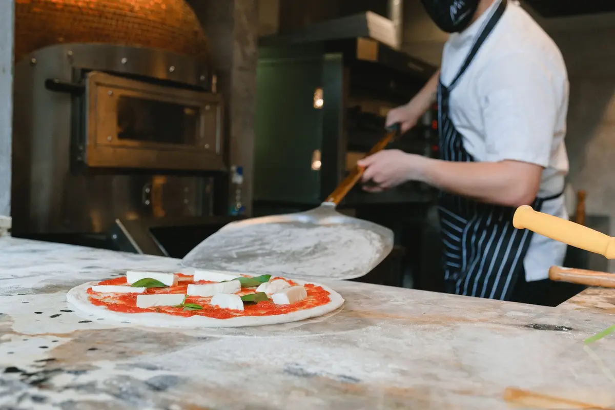 Pizza maker sliding a fresh pizza toward a pizzeria oven